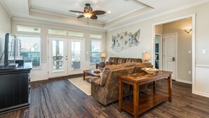 A spacious living room with a dark wood floor, a brown leather sofa, a wooden coffee table, and a ceiling fan.