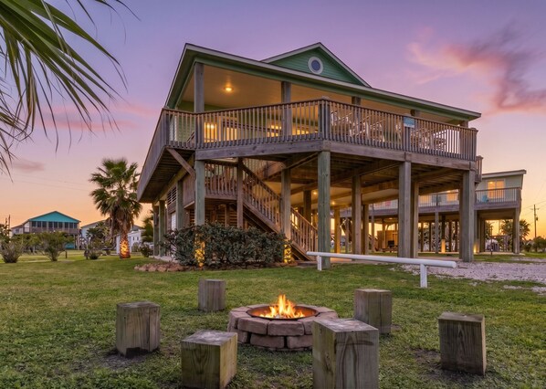 A large two-story house with a balcony, a fire pit, and a well-maintained lawn.