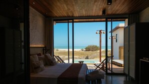 A bedroom with a large bed, a bench, and a view of the beach and ocean.