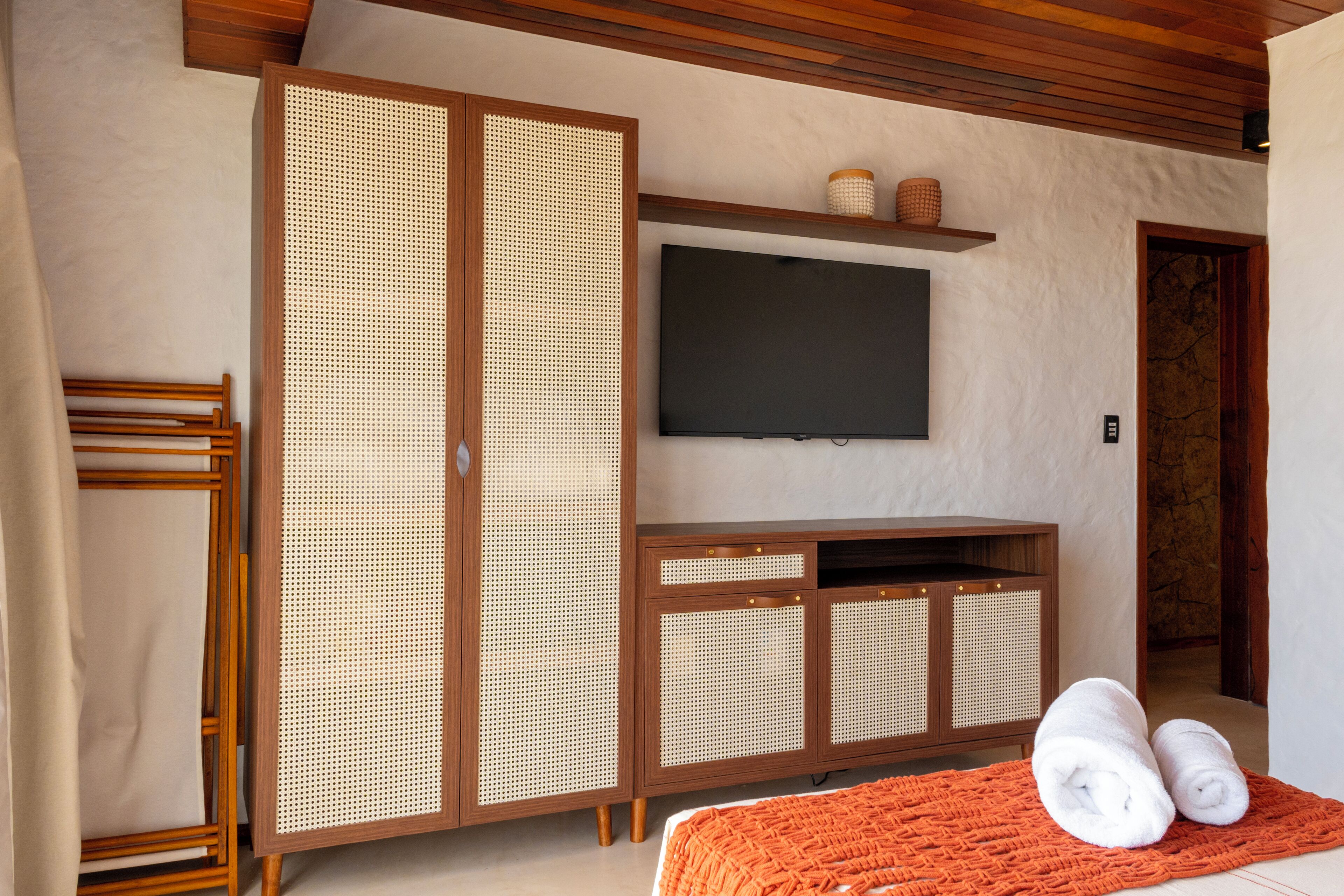 A room with a wooden wardrobe, a flat-screen TV, and a bed with rolled towels.
