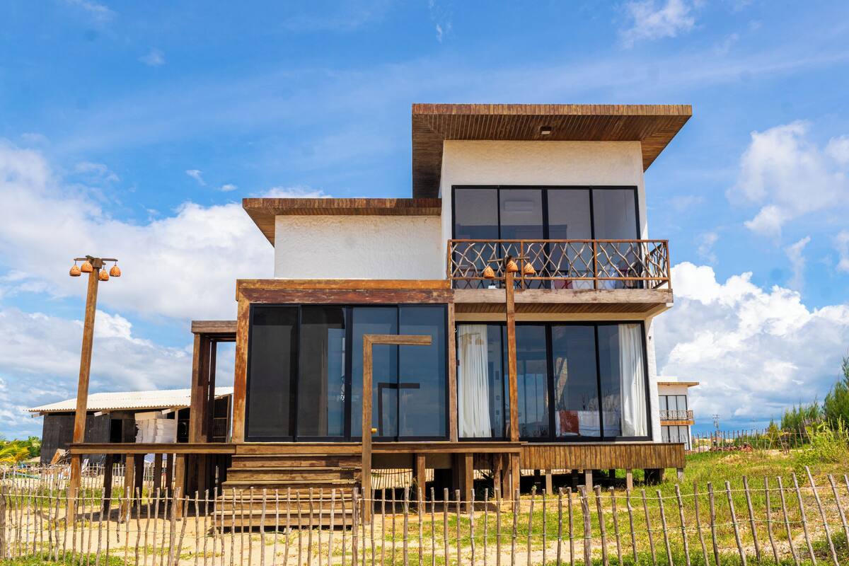 Una casa moderna de dos pisos con amplios ventanales, un balcón y una terraza de madera.