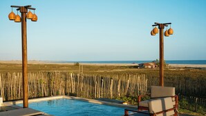 A pool area with lounge chairs, a wooden deck, and a view of the beach.