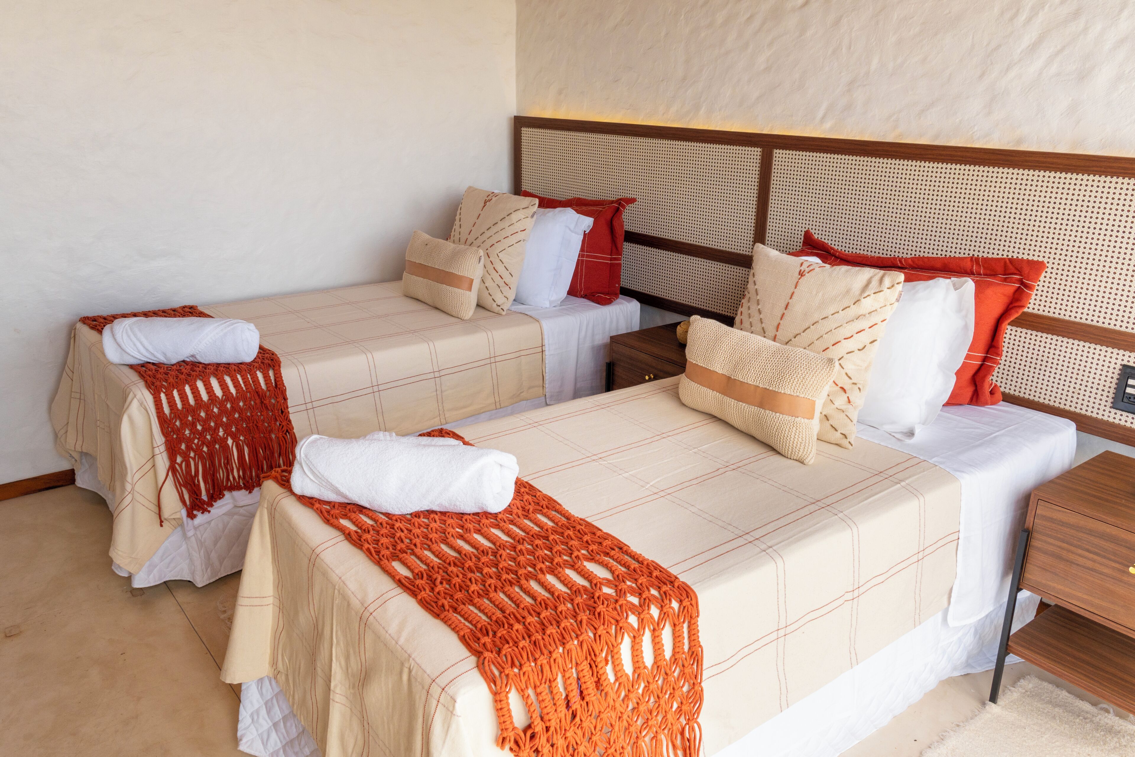 Ein Hotelzimmer mit zwei Betten, jeweils mit Kopfstütze, einem hölzernen Nachttisch und einer weißen Wand.