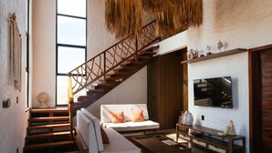 A modern living room with a staircase, a sofa, a coffee table, and a TV mounted on the wall.