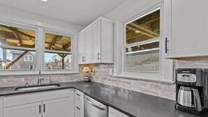 A kitchen with white cabinets, a black countertop, a coffee maker, and a window with a view of the outside. - Normandy Beach Retreat! Cozy 3BR Apartment, Just Steps from the sand (Lavallette)