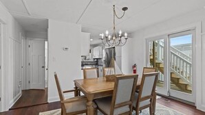 A dining area with a wooden table and chairs, a chandelier, and a view of a staircase leading to a balcony. - Normandy Beach Retreat! Cozy 3BR Apartment, Just Steps from the sand (Lavallette)