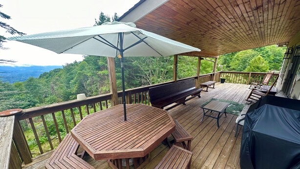 Eine Holzterrasse mit Tisch, Bänken, einem Grill und einem Sonnenschirm.