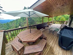 Un terrazzo in legno con tavolo e panche, un barbecue e un ombrellone.