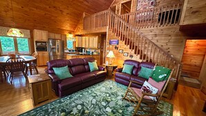 Ein gemütliches Blockhaus-Interieur mit einer Holztreppe, einer Essecke, einer Küche und einem Wohnzimmer mit Sofa und Schaukelstuhl.