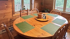 Ein Esszimmer aus Holz mit einem runden Tisch, grünen Platzsets und einer hängenden Leuchte aus Buntglas.