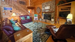 Ein gemütliches Blockhaus-Interieur mit Ledersofa, Kamin, Holztreppe und einer Wand aus Naturstein.