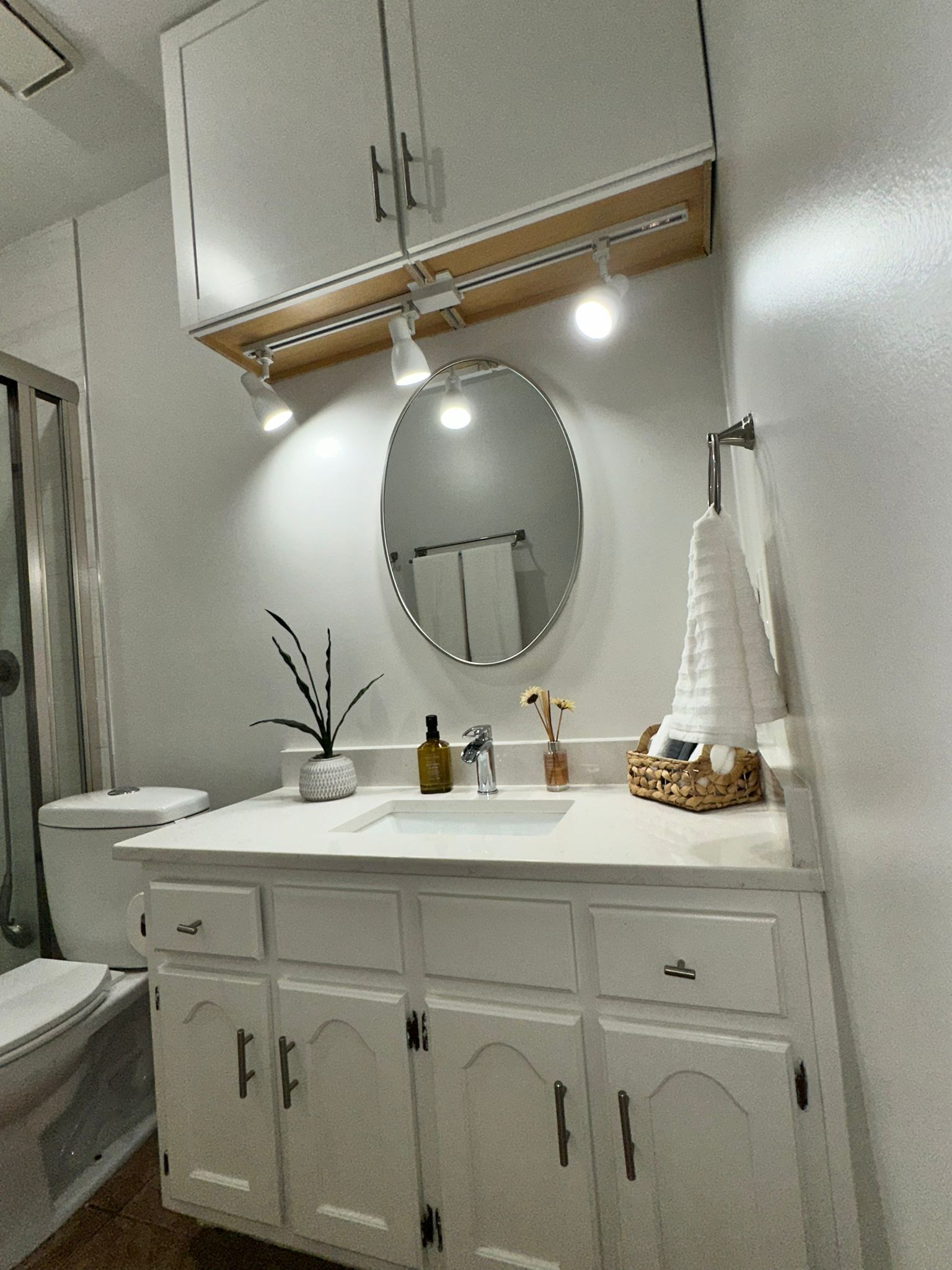 A bathroom with a white vanity, a round mirror, and a towel rack.