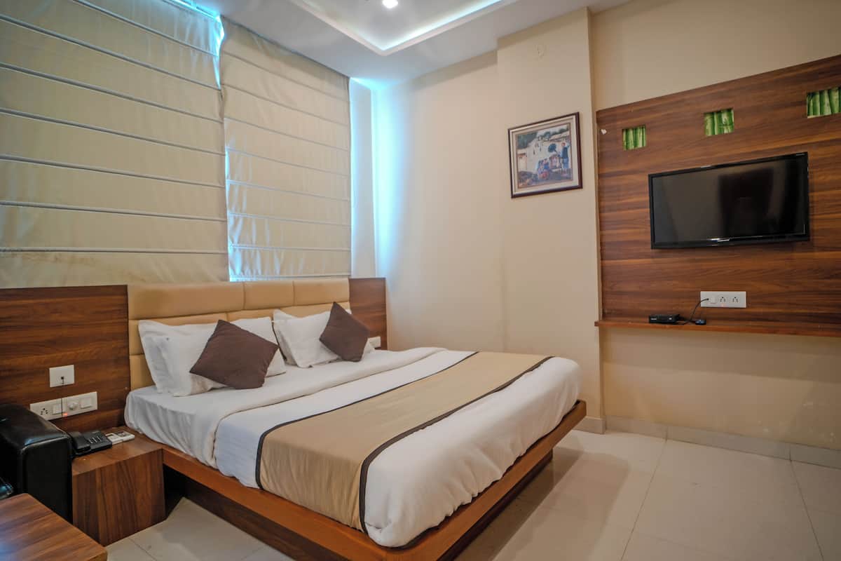 Ein modernes Hotelzimmer mit einem großen Bett, einem Holzkopfteil, einem an der Wand befestigten Flachbildfernseher und einem Nachttisch mit Telefon und Fernbedienung.