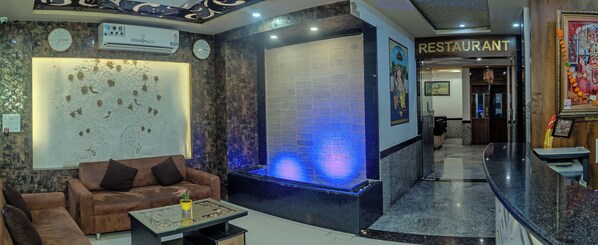 A lobby with a reception desk, a brown sofa, a decorative wall, and a clock.