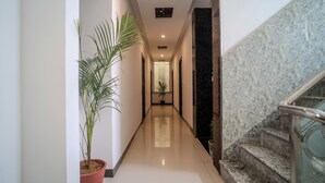A hallway with a potted plant, a staircase with a glass railing, and a polished floor.