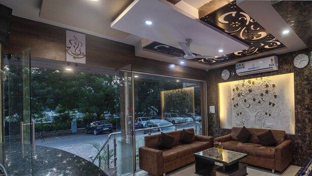 A modern lobby with two brown sofas, a glass partition, and a decorative wall with a clock and air conditioning unit.