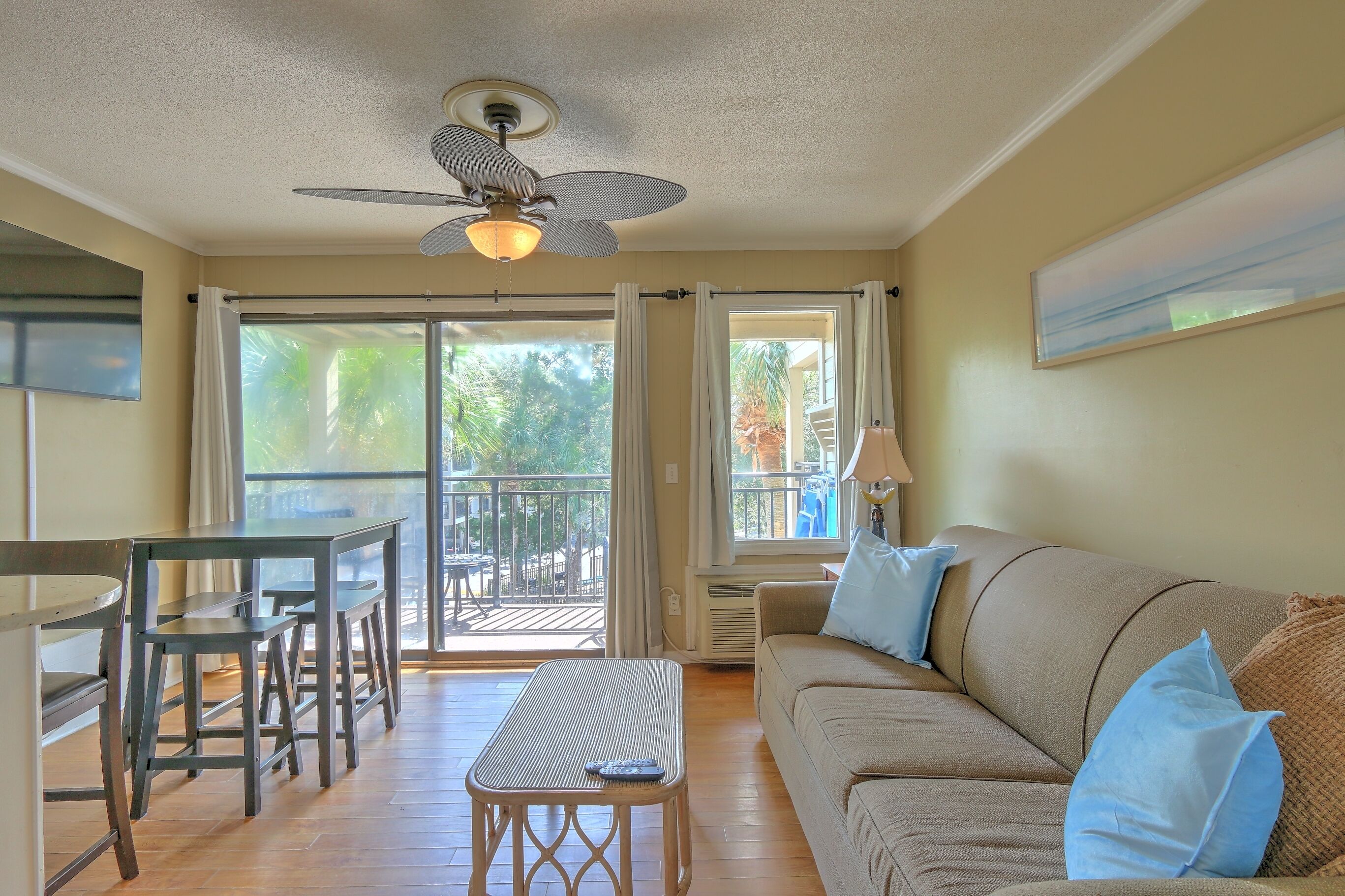 A living room with a sofa, a table, and chairs, a ceiling fan, and a view through a sliding door to an outdoor area.