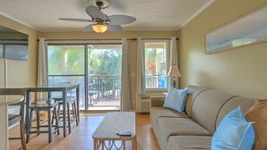 A living room with a sofa, a table, and chairs, a ceiling fan, and a view through a sliding door to an outdoor area.