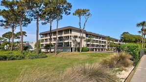 A multi-story building with balconies, surrounded by grass and trees.