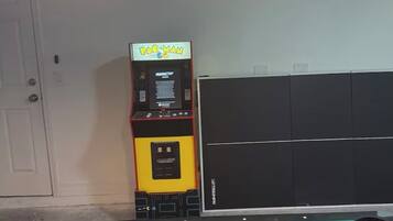 A pool table with overhead lighting, a Pac-Man arcade machine, and a black cabinet.