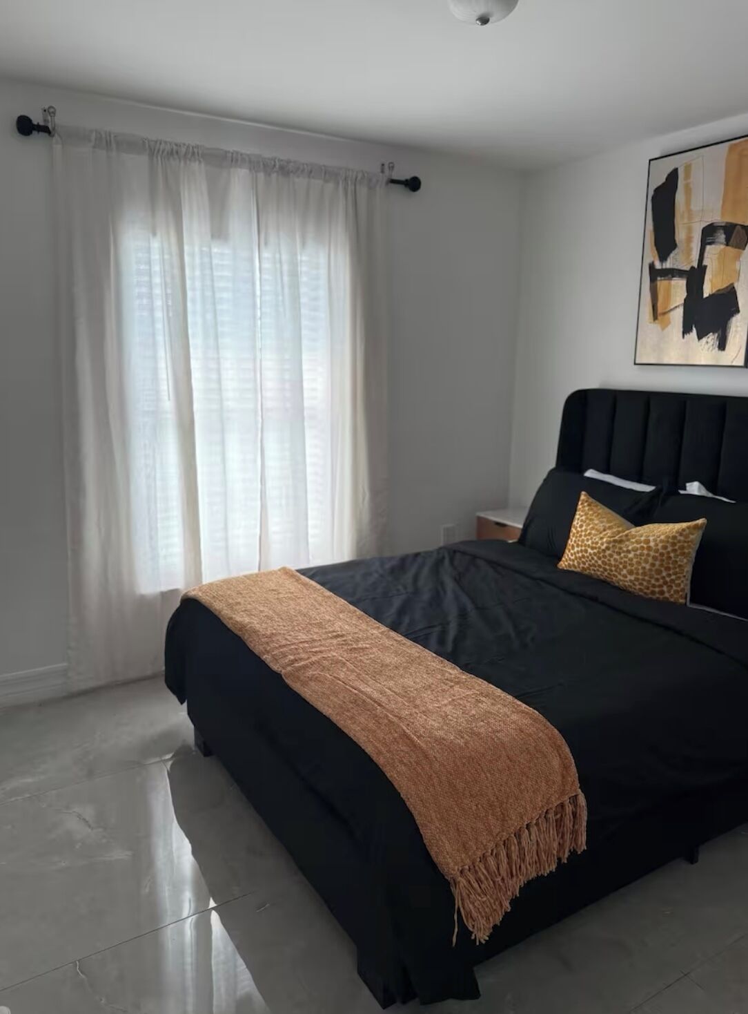 A modern bedroom with a black bed, a beige throw blanket, and a giraffe-patterned pillow.