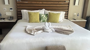 Une chambre d’hôtel avec un grand lit, deux tables de chevet, une petite table, un banc et une tête de lit en bois.