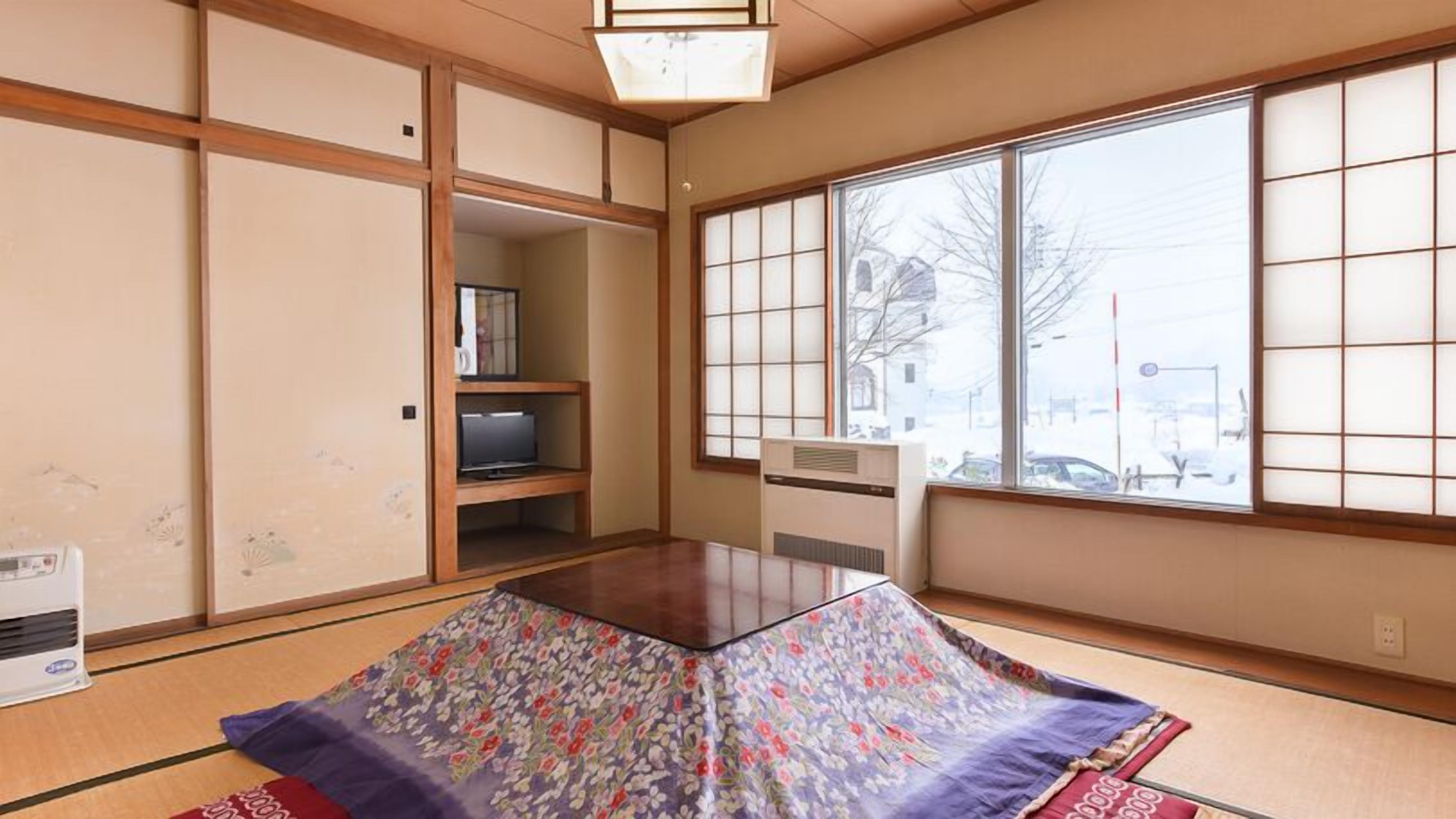 A traditional Japanese room with tatami flooring, sliding doors, a television on a low shelf, and a large window with a view of the street.