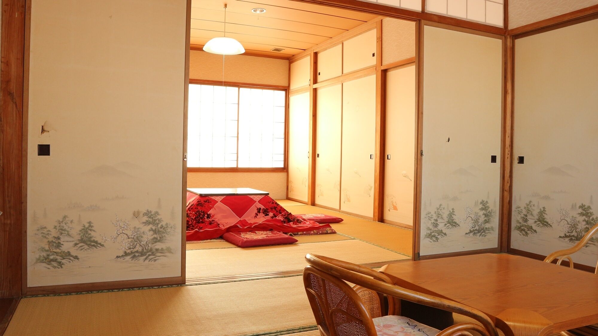 Une pièce de style japonais traditionnel, avec un sol recouvert de tatamis, des portes coulissantes et une basse table en bois entourée de chaises.