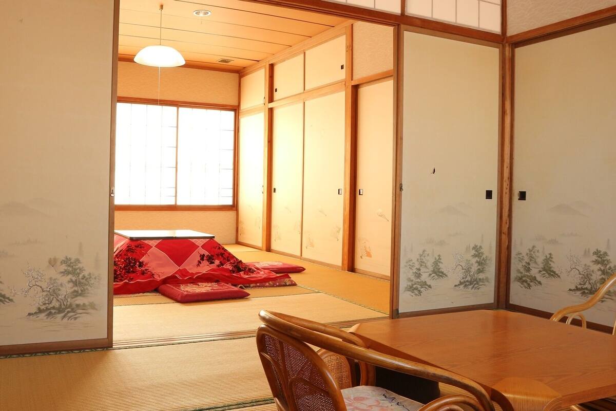 A traditional Japanese room with tatami flooring, sliding doors, and a low wooden table with chairs.