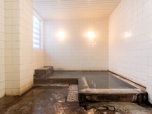 A traditional Japanese onsen with a stone bath, tiled walls, and a window for natural light. - akakura onsen eho ryokan (Myoko)