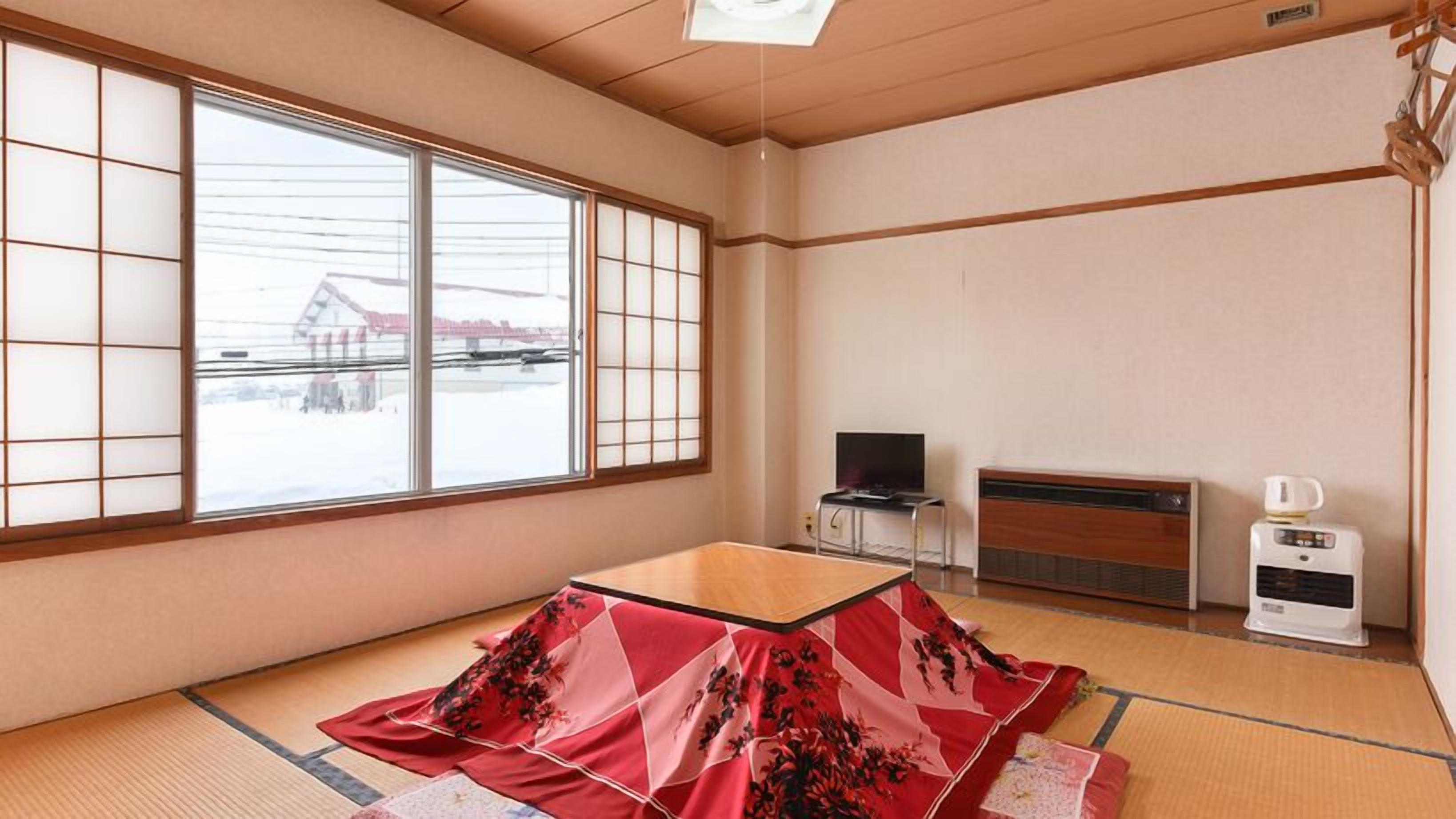 A traditional Japanese room with tatami flooring, a low wooden table, a television, and a heater.