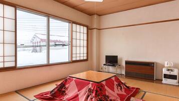 Een traditionele Japanse kamer met tatami vloerbedekking, een futonbed, een televisie op een standaard en een verwarming.