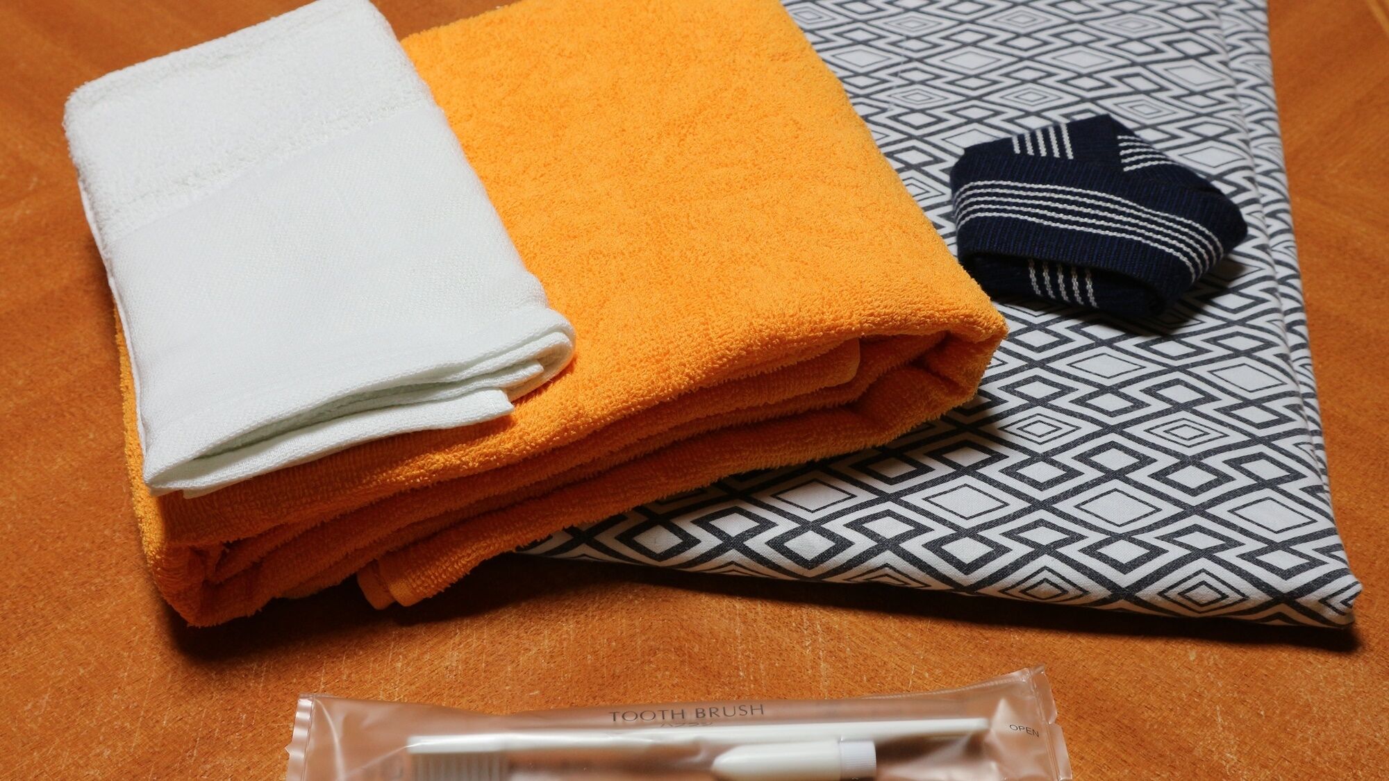 Une serviette blanche et orange, soigneusement pliée, un coussin à motifs et une brosse à dents dans un étui en plastique transparent.