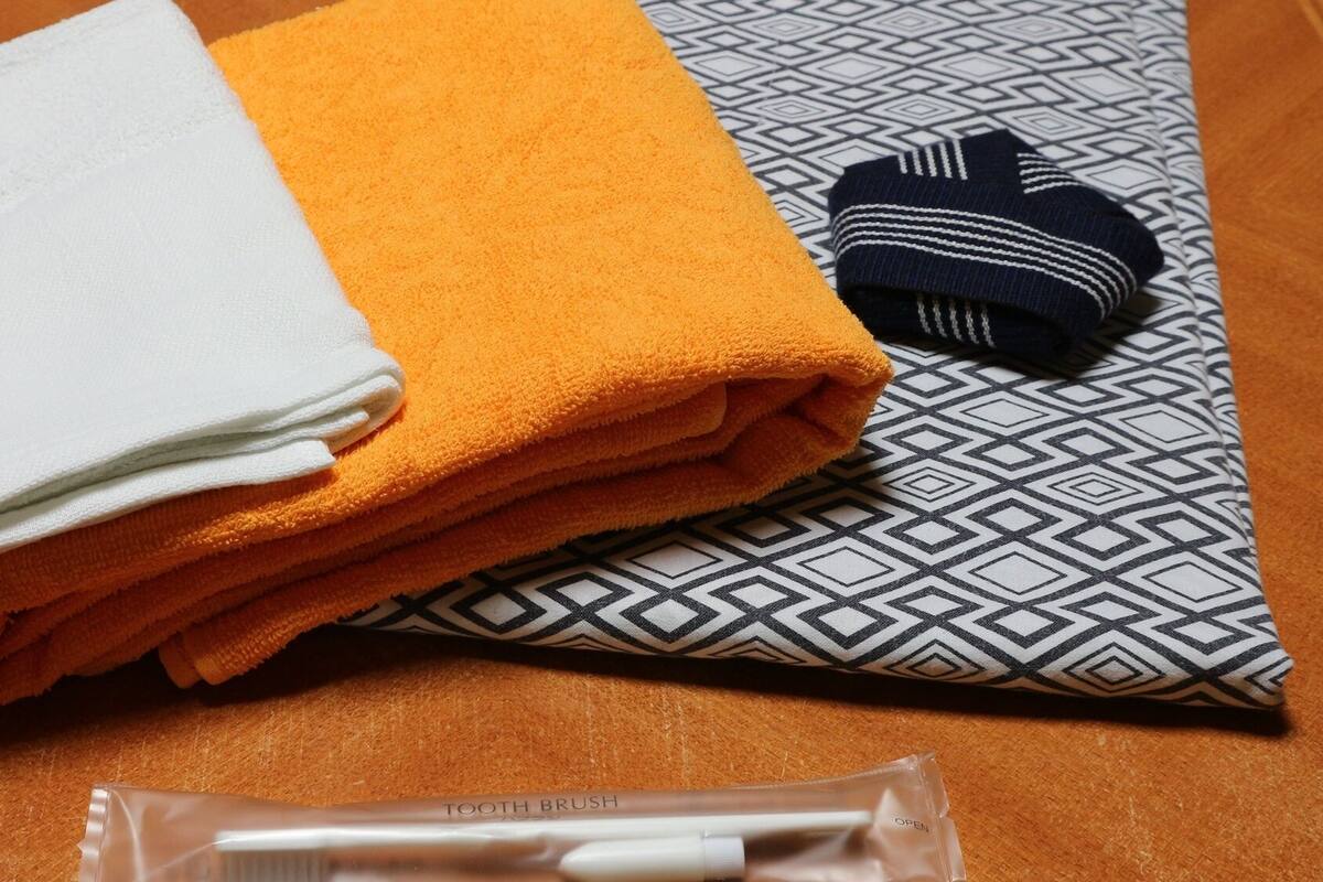 A neatly folded white and orange towel, a patterned pillow, and a toothbrush in a clear plastic case.