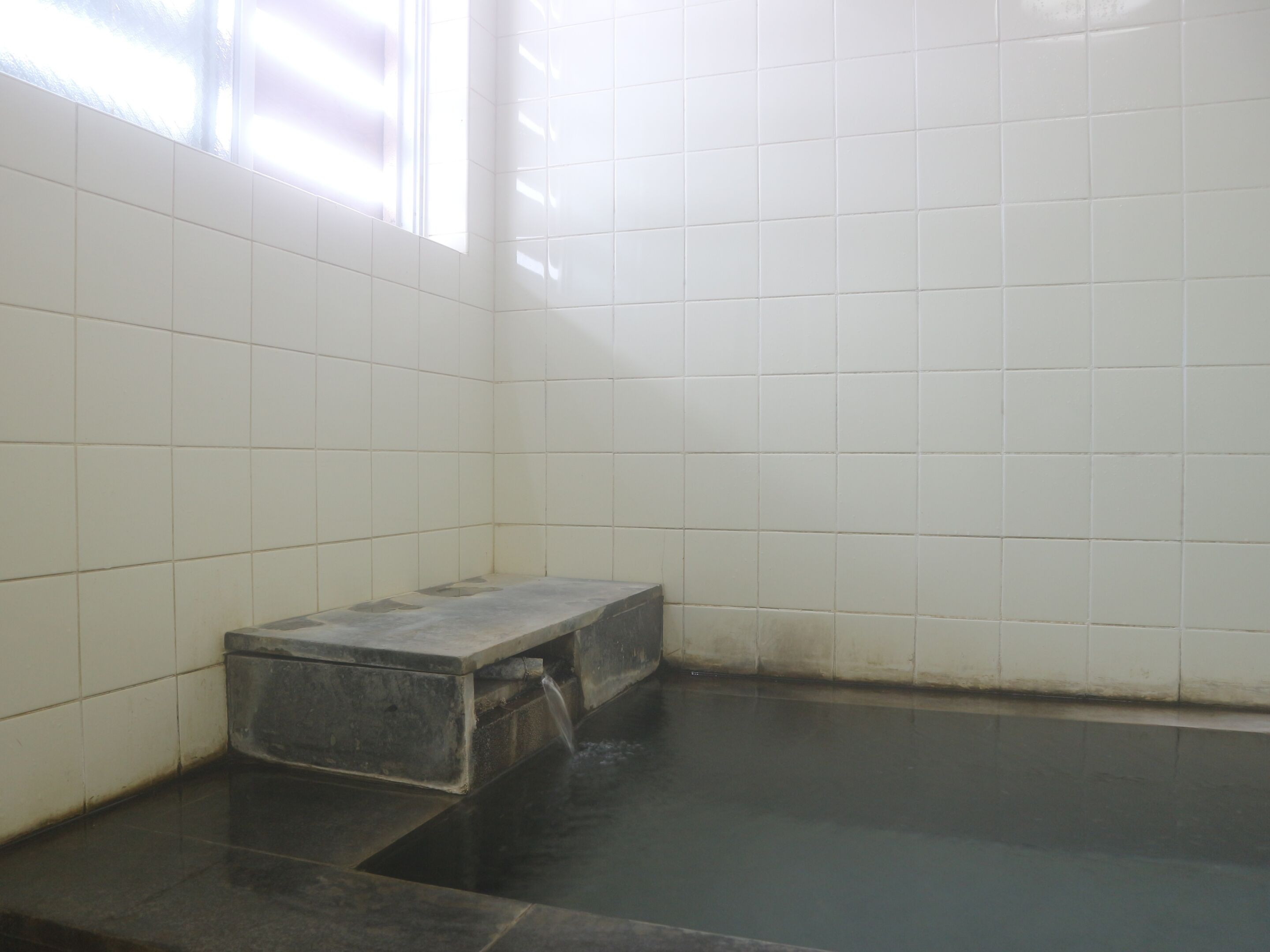 A bathroom with white tiled walls, a black bathtub, and a small bench.