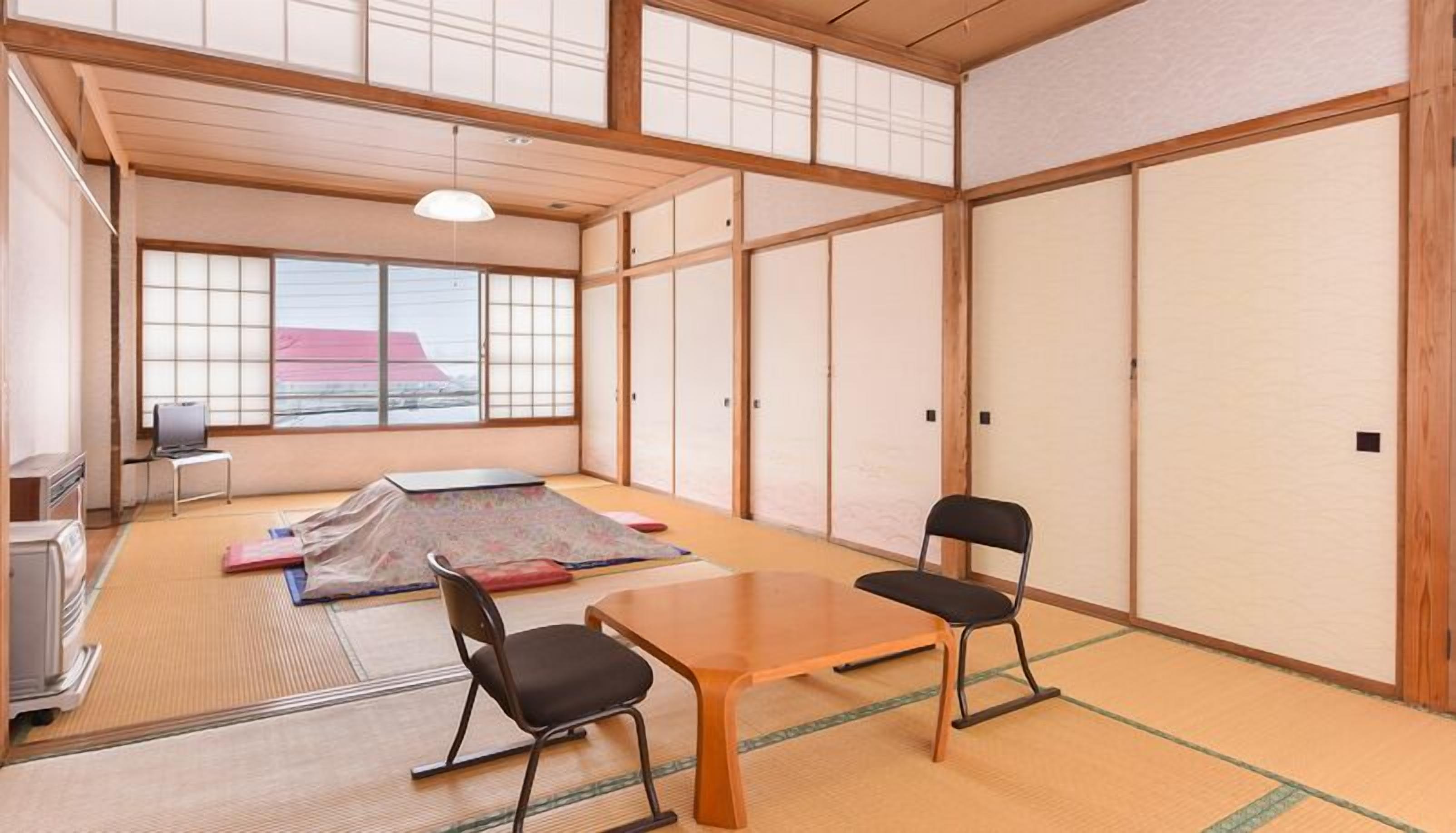 A traditional Japanese room with tatami flooring, a low table, two chairs, a futon, and sliding doors.