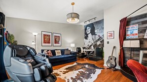 Ein modernes Wohnzimmer mit Massagesessel, blauem Sofa, Kuhfellteppich und Gitarre.