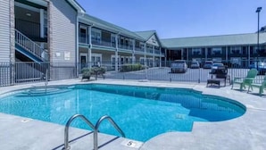 Hotel med swimmingpool, udendørs siddepladser og parkeringsareal.