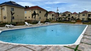 Piscina com espreguiçadeiras, cercada por edifícios de apartamentos com telhados vermelhos.