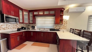 Cozinha moderna com armários de madeira escura, bancada branca e micro-ondas embutido.