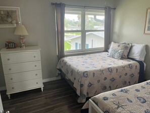 A bedroom with a bed, a dresser, a window with curtains, and a view of a house and greenery outside. - Charming 2 bdrm 1.5 bath villa 100 yards to Three Sisters Springs (Crystal River)