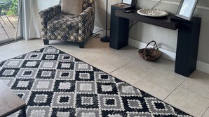 Una sala de estar con un sillón estampado, una lámpara de pie, un televisor de pantalla plana y un escritorio con una computadora y objetos decorativos.