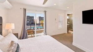 A hotel room with a bed, a ceiling fan, a TV mounted on the wall, and a view of the outside balcony.