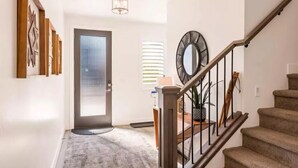A modern hallway with a staircase, a door with a frosted glass panel, and a wall-mounted mirror.