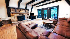 Un salon chaleureux avec une cheminée en pierre, des canapés en cuir et une grande fenêtre donnant sur le paysage extérieur.