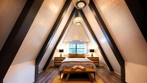 Une chambre avec un plafond en pente, un lit avec une banquette, deux tables de chevet et une fenêtre avec des rideaux.