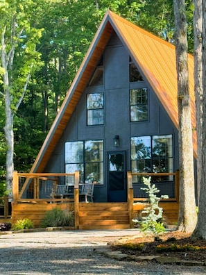 A modern cabin with a wooden deck and large windows, surrounded by trees. - A-frame Retreat on Private Pond (Oneonta)