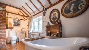 A bathroom with a large bathtub, wooden beams on the ceiling, and a window with curtains. - Farm View suite, Kelsale (Kelsale)