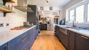A modern kitchen with dark cabinetry, a central island, and a large window providing natural light. - Farm View suite, Kelsale (Kelsale)