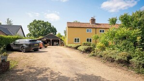 A residential property with a gravel driveway, a garage, and a two-story house with a tiled roof. - Farm View suite, Kelsale (Kelsale)